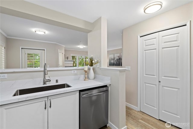kitchen featuring stainless steel dishwasher, a sink, light wood finished floors, and crown molding