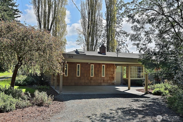 rear view of property featuring a shingled roof, a chimney, and an attached carport