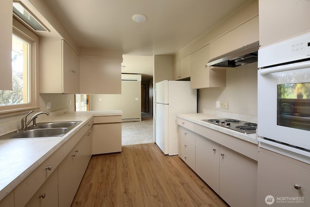 kitchen with light wood finished floors, light countertops, white appliances, and a sink