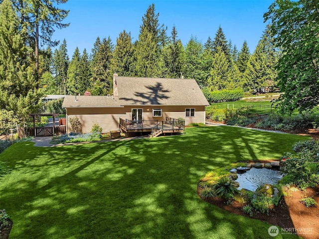 rear view of house featuring a lawn, a deck, fence, and a small pond