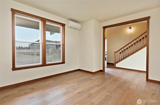 unfurnished room with stairs, baseboards, light wood-style floors, and a wall unit AC
