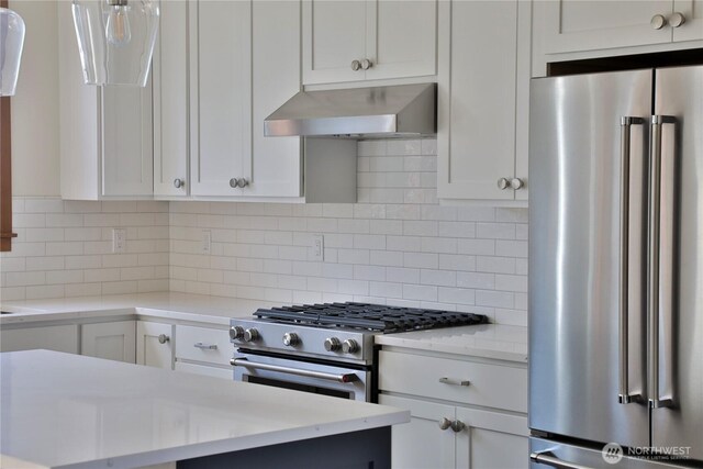 kitchen featuring wall chimney exhaust hood, backsplash, premium appliances, and white cabinetry