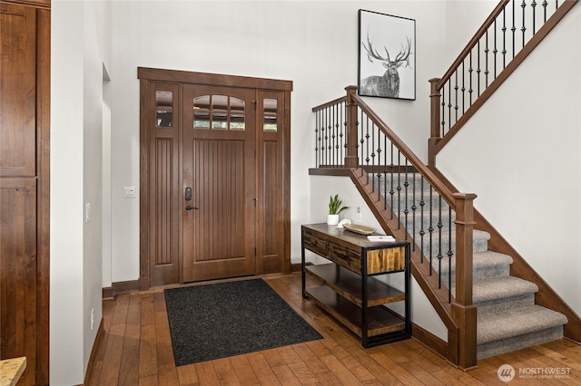 foyer entrance with wood-type flooring, baseboards, a high ceiling, and stairway