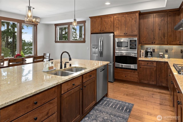 kitchen with decorative backsplash, hanging light fixtures, light wood-type flooring, a sink, and stainless steel appliances