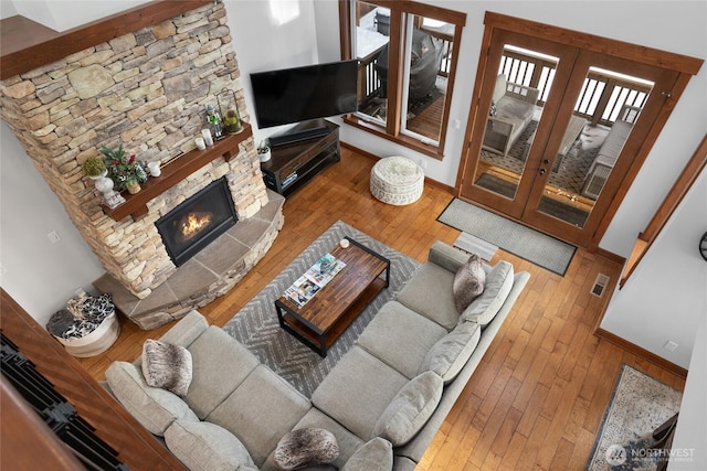 living room with visible vents, a stone fireplace, baseboards, hardwood / wood-style flooring, and french doors
