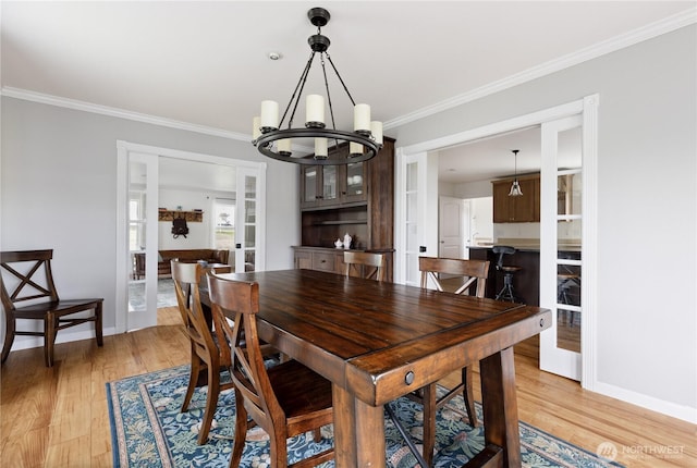 dining space featuring an inviting chandelier, ornamental molding, light wood-style flooring, and baseboards
