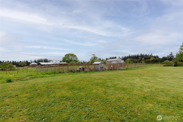 view of yard with an outdoor structure, an exterior structure, fence, and a rural view