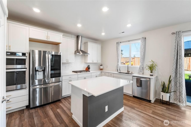 kitchen with wall chimney range hood, stainless steel appliances, dark wood-style floors, and a sink