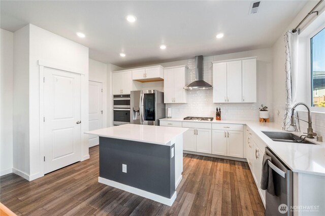 kitchen with a sink, dark wood-style flooring, appliances with stainless steel finishes, and wall chimney range hood