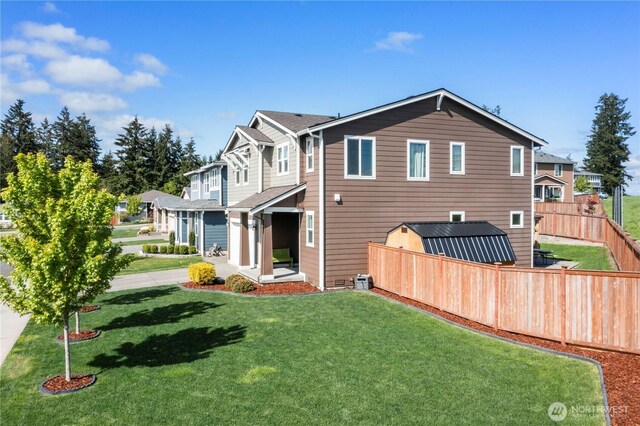 back of property with fence, a lawn, and a storage shed