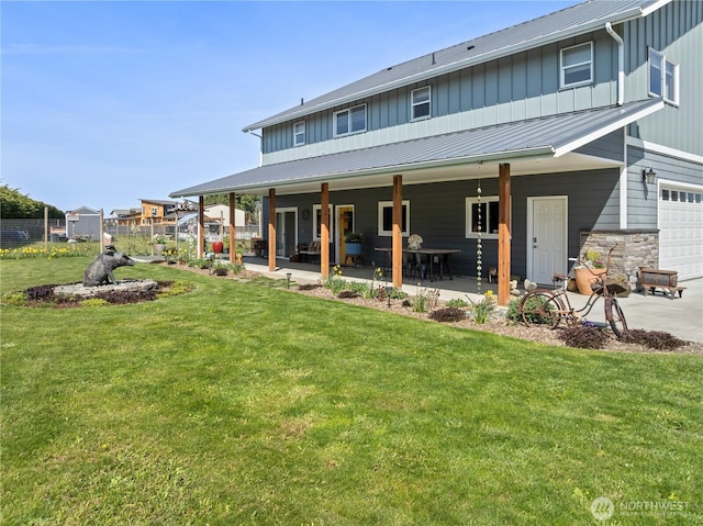 back of property with a patio area, board and batten siding, an attached garage, a yard, and metal roof