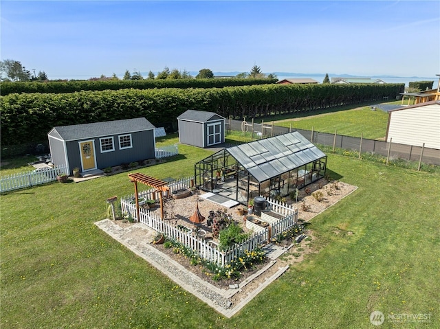 view of yard with a greenhouse, a fenced backyard, a rural view, an outbuilding, and a storage unit