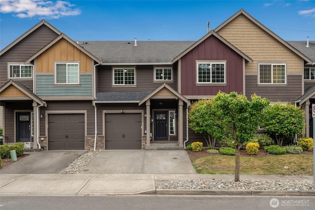 view of front of property featuring board and batten siding, driveway, a shingled roof, an attached garage, and stone siding