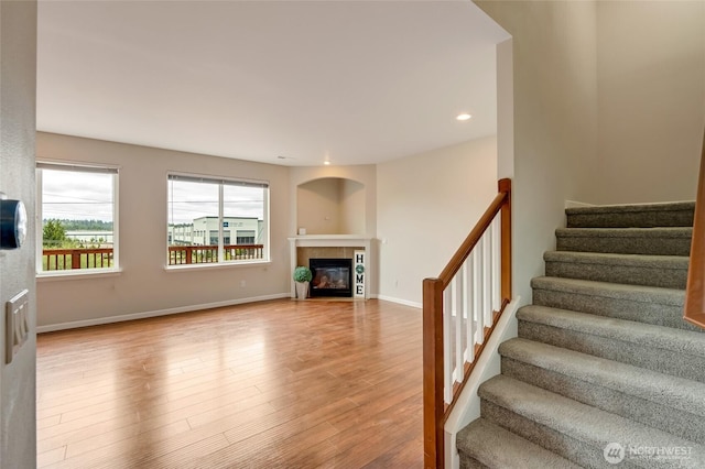 unfurnished living room with stairway, a tiled fireplace, wood finished floors, baseboards, and recessed lighting