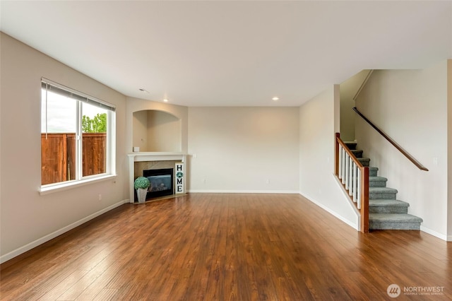unfurnished living room with wood finished floors, a tiled fireplace, stairway, and recessed lighting
