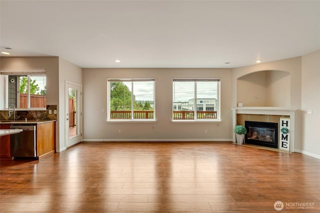 unfurnished living room featuring recessed lighting, wood finished floors, a tiled fireplace, a sink, and baseboards