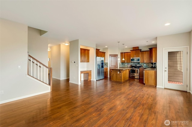 kitchen featuring stainless steel appliances, brown cabinets, a center island, open floor plan, and dark wood-style floors