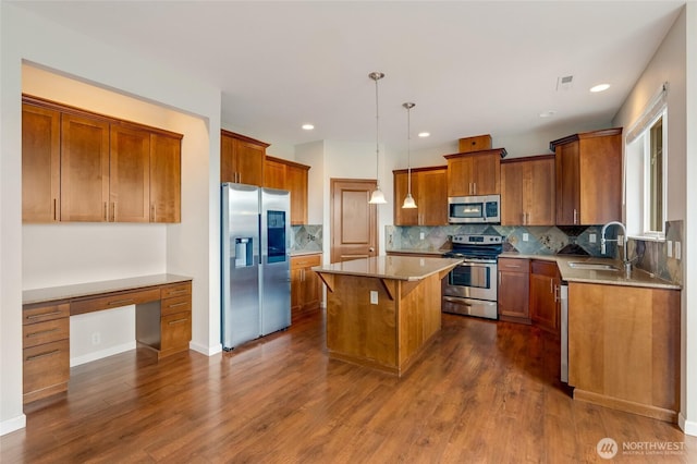 kitchen with appliances with stainless steel finishes, a sink, a center island, brown cabinetry, and dark wood-type flooring