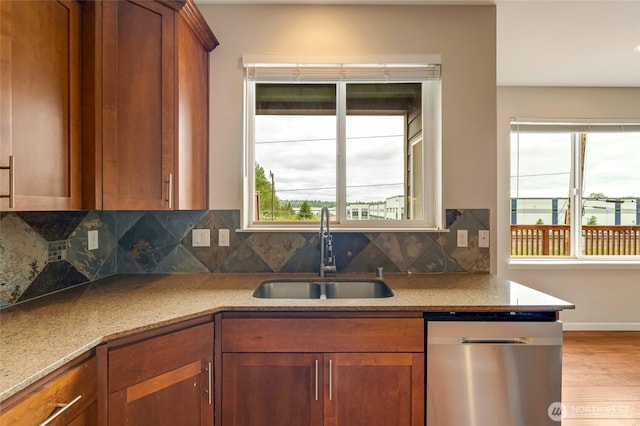kitchen featuring stainless steel dishwasher, a sink, wood finished floors, brown cabinetry, and backsplash