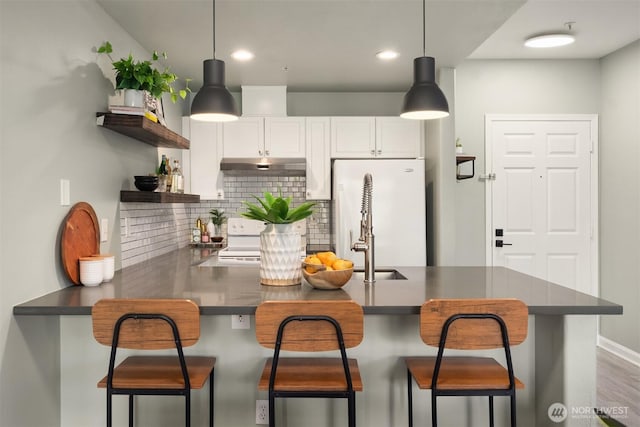 kitchen featuring open shelves, dark countertops, under cabinet range hood, and white appliances