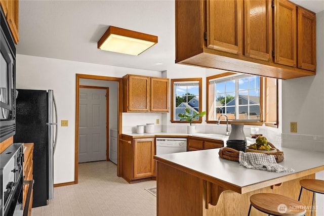 kitchen with a peninsula, a sink, freestanding refrigerator, dishwasher, and light countertops