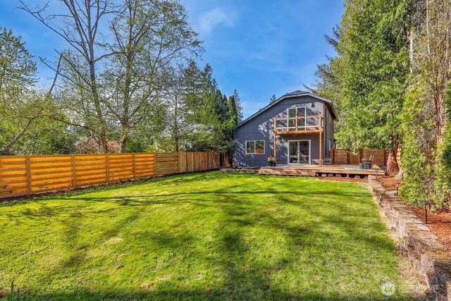 rear view of property with a fenced backyard, a wooden deck, a balcony, and a lawn