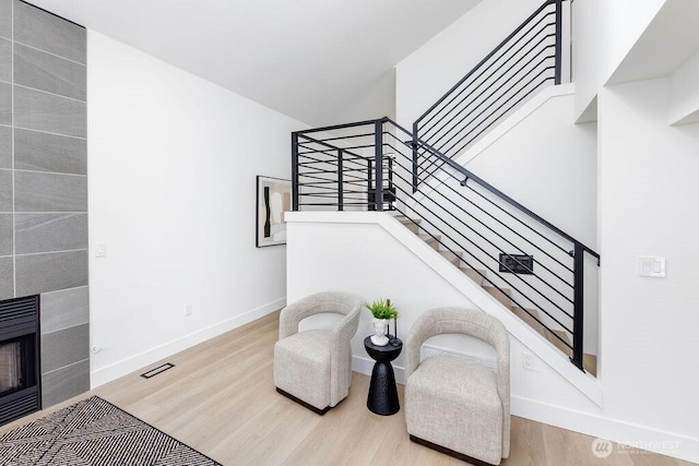 living area with stairway, wood finished floors, a tile fireplace, baseboards, and visible vents