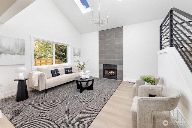 living room featuring high vaulted ceiling, wood finished floors, a skylight, a tile fireplace, and a notable chandelier