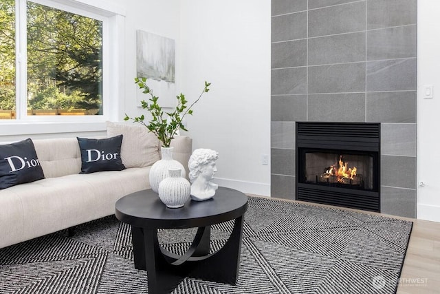 living area featuring plenty of natural light, a tile fireplace, baseboards, and wood finished floors