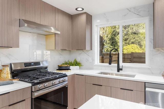 kitchen with a sink, modern cabinets, light countertops, under cabinet range hood, and appliances with stainless steel finishes