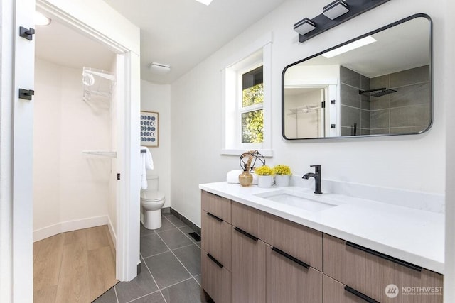 bathroom with tile patterned floors, toilet, vanity, a walk in closet, and baseboards
