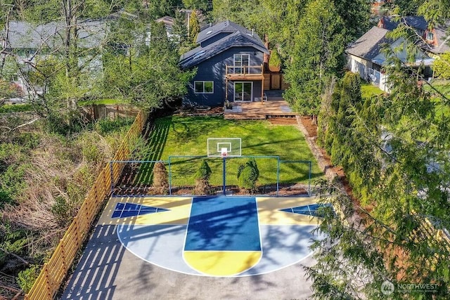 view of basketball court featuring basketball hoop, a lawn, and fence
