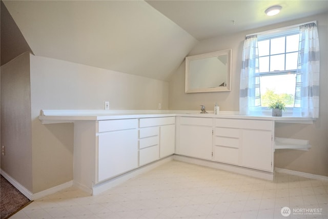 interior space featuring a healthy amount of sunlight, baseboards, vaulted ceiling, and white cabinetry