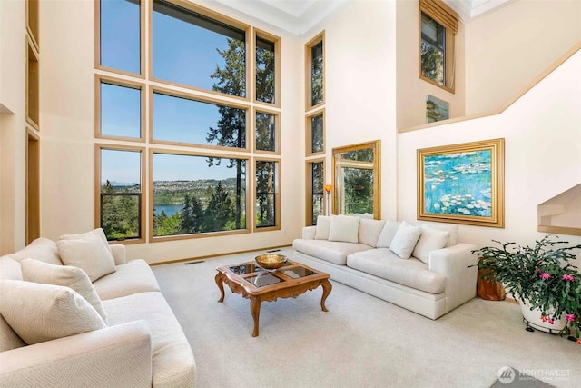 carpeted living area with a towering ceiling, healthy amount of natural light, and a water view