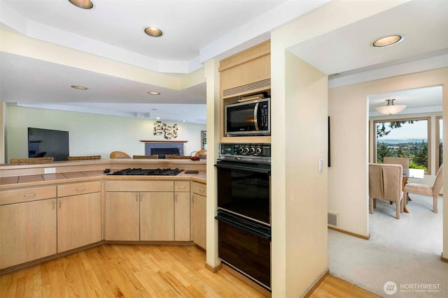 kitchen with light brown cabinetry, black appliances, a fireplace, open floor plan, and recessed lighting