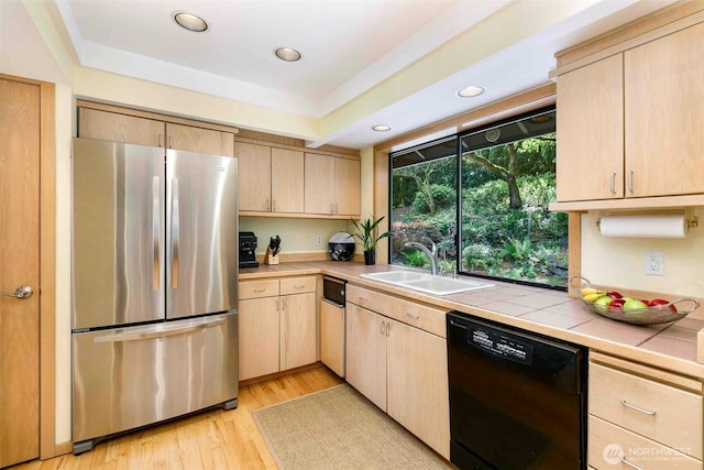 kitchen with freestanding refrigerator, dishwasher, a sink, light brown cabinetry, and tile countertops