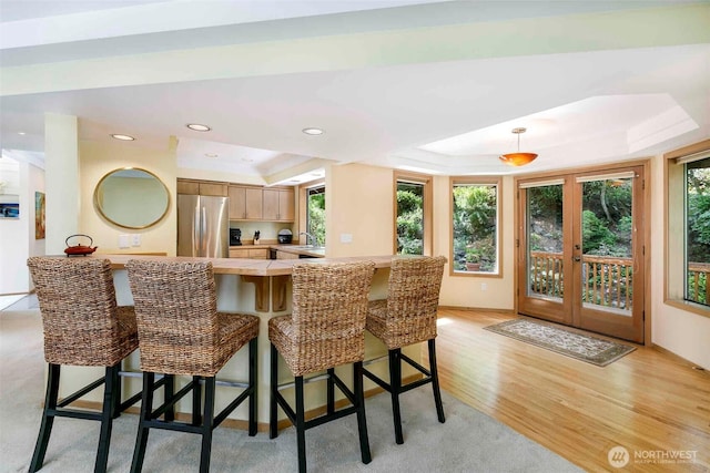 kitchen featuring freestanding refrigerator, a raised ceiling, light countertops, light wood finished floors, and a peninsula