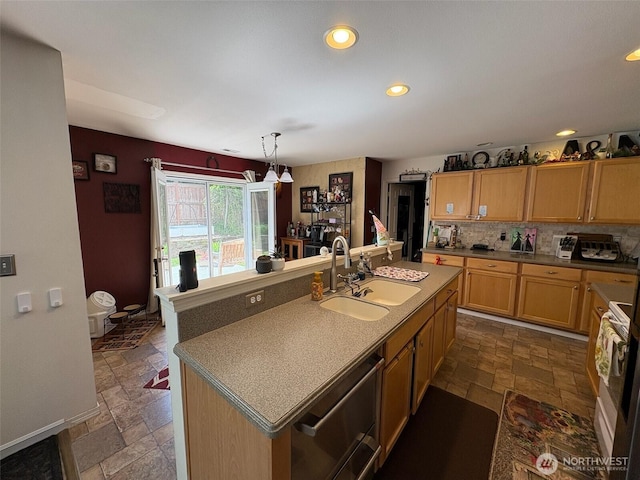 kitchen featuring backsplash, a kitchen island with sink, a sink, and stone tile flooring