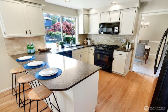 kitchen with a peninsula, dark countertops, white cabinetry, a sink, and black appliances