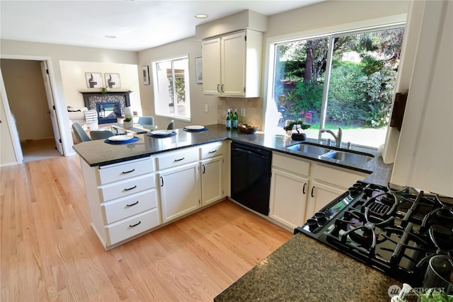 kitchen with a sink, gas stove, light wood finished floors, a peninsula, and black dishwasher