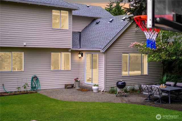rear view of house featuring a patio, a shingled roof, and a yard