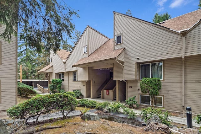 rear view of property featuring stairway, a shingled roof, and a patio area
