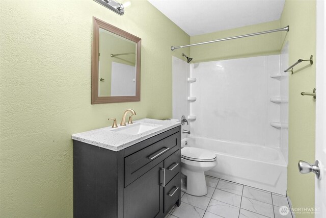 full bath with a textured wall, vanity, toilet, marble finish floor, and shower / washtub combination