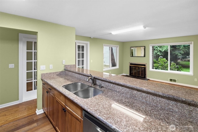 kitchen featuring visible vents, a glass covered fireplace, wood finished floors, a sink, and a wealth of natural light