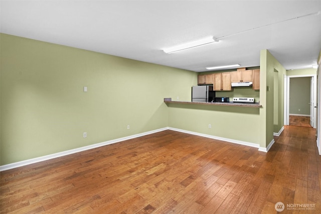kitchen featuring range with electric stovetop, baseboards, freestanding refrigerator, under cabinet range hood, and hardwood / wood-style floors