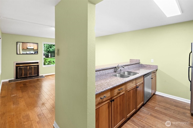 kitchen featuring a glass covered fireplace, hardwood / wood-style floors, baseboards, a sink, and stainless steel appliances