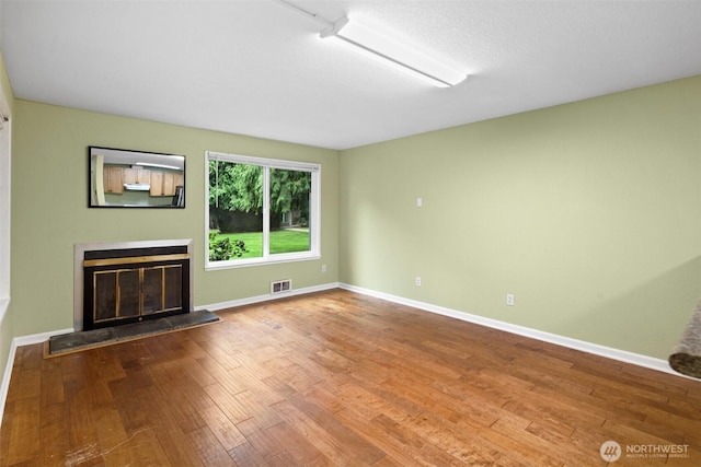 unfurnished living room featuring baseboards, visible vents, a glass covered fireplace, and wood finished floors