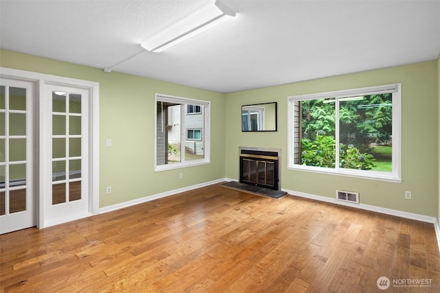 unfurnished living room featuring visible vents, baseboards, a glass covered fireplace, and wood finished floors