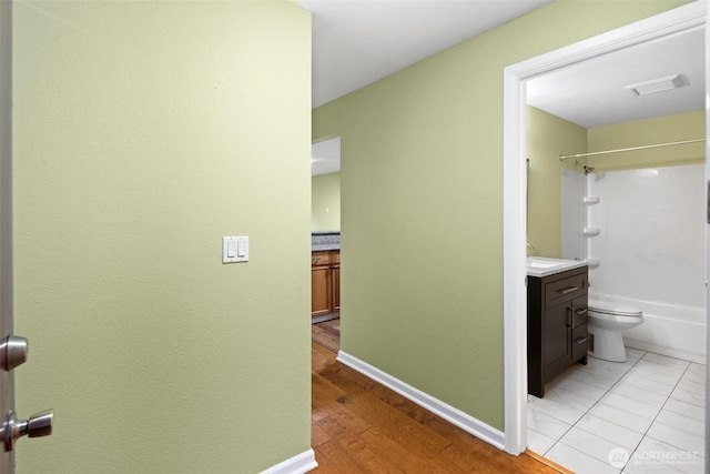 hall featuring a sink, baseboards, light wood-type flooring, and visible vents