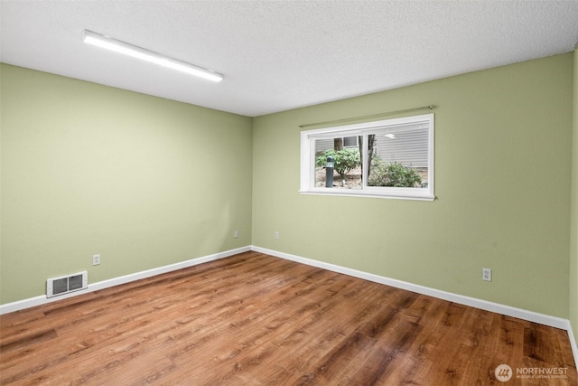 empty room with a textured ceiling, baseboards, visible vents, and wood finished floors